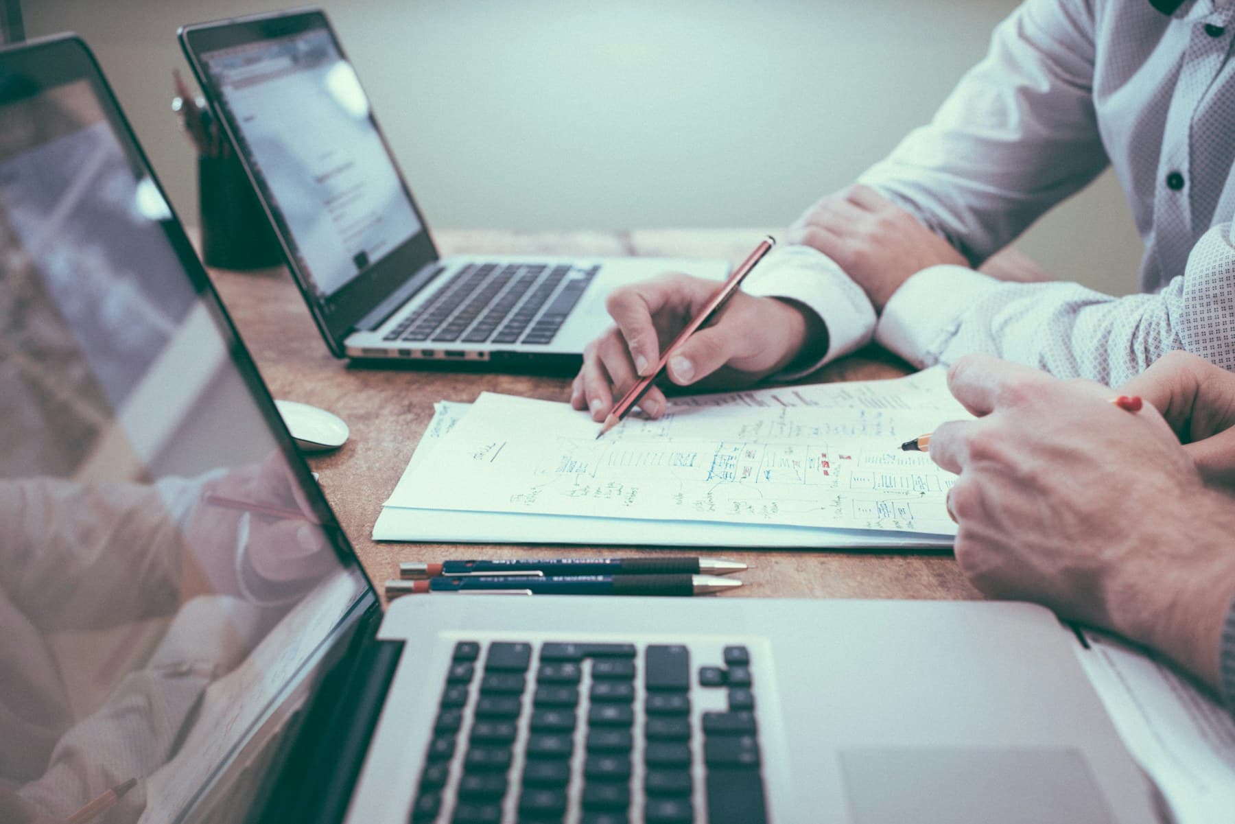 Hands and laptops around a meeting table mid-discussion